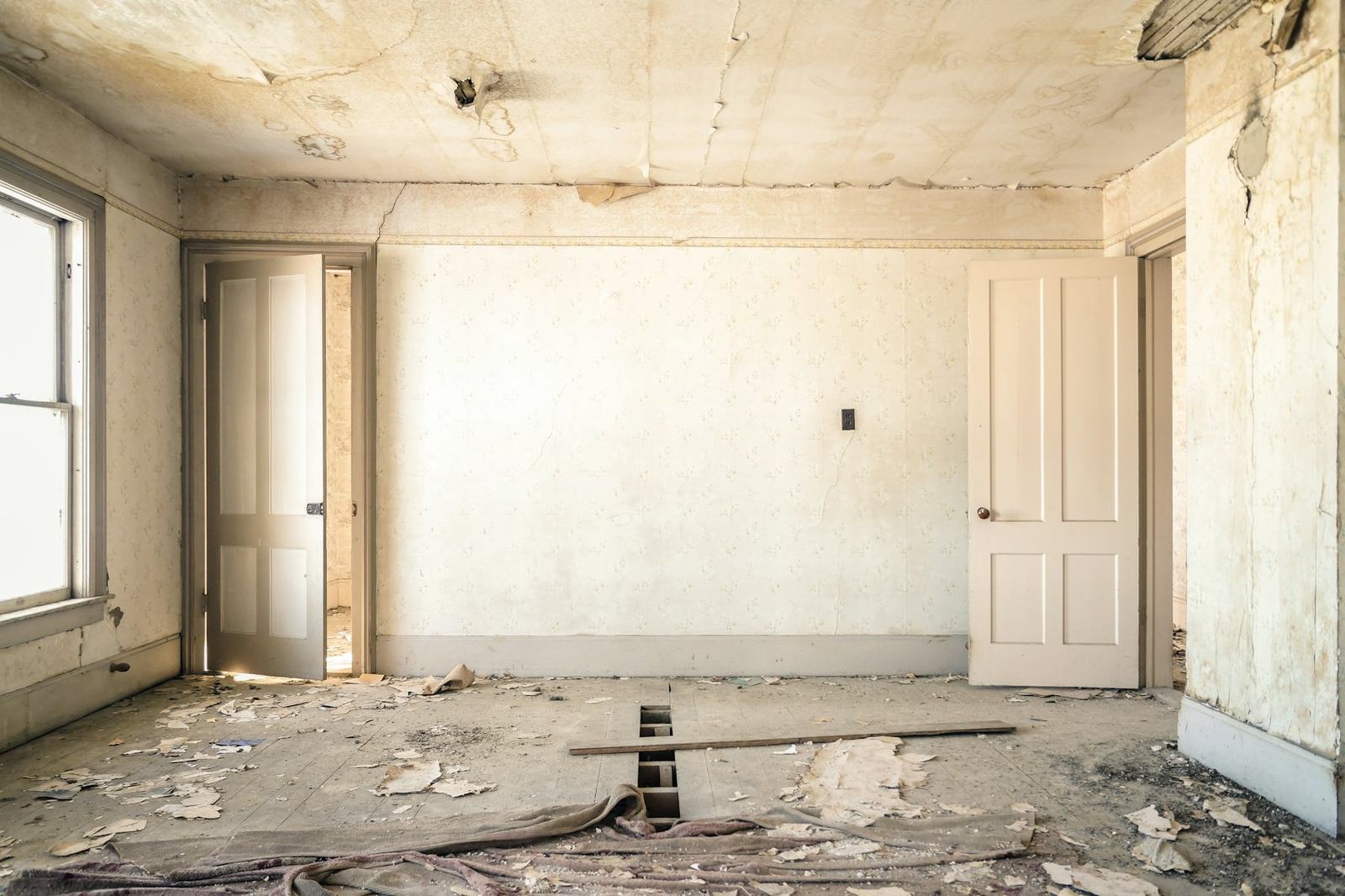 Pièce vide avant rénovation, murs décollés et sol à reprendre