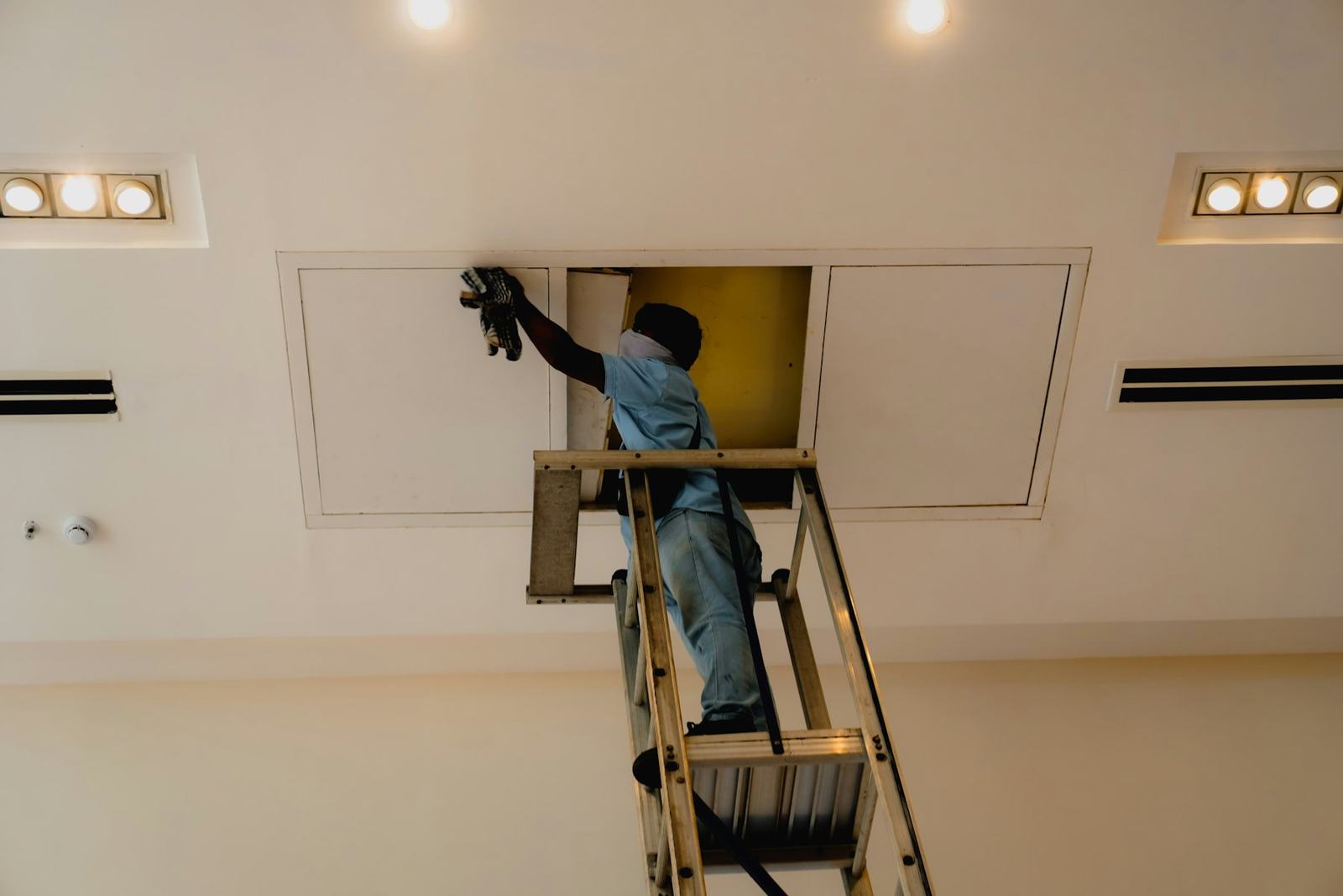 Ouvrier sur un escabeau travaillant au plafond d'une pièce lumineuse